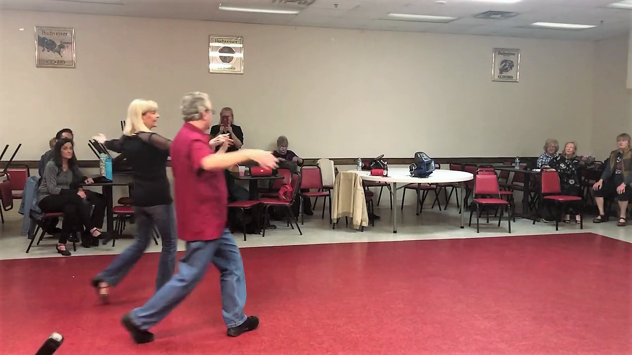 A group of people are dancing in a room with tables and chairs