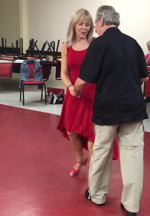 A woman in a red dress is dancing with a man in a black shirt