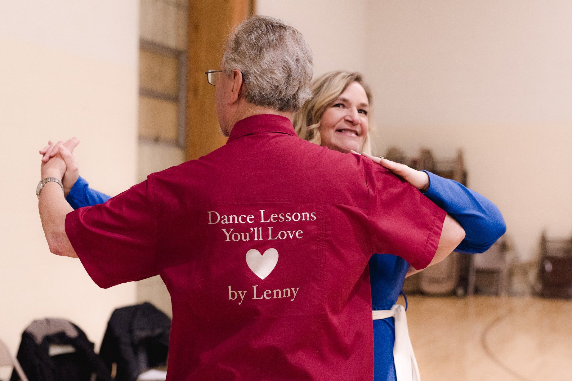 A man wearing a red shirt that says dance lessons you 'll love is dancing with a woman.