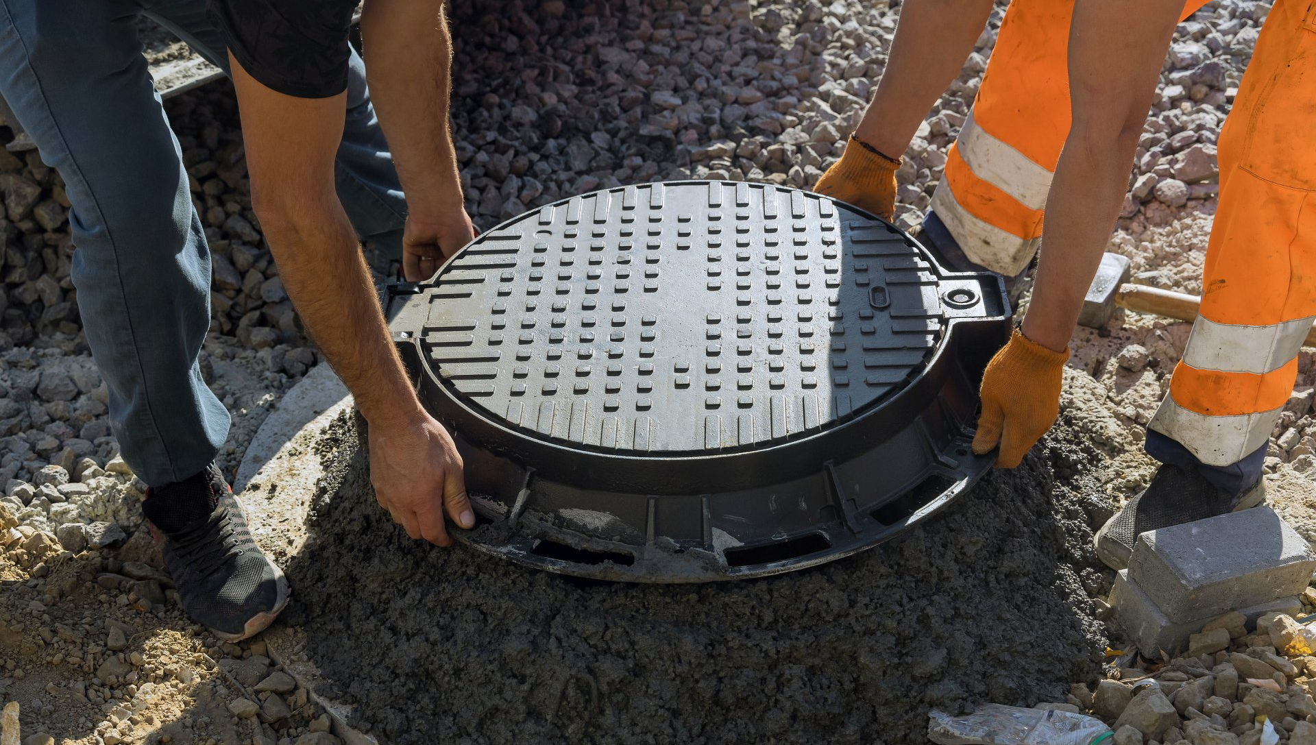 Two men are working on a manhole cover on a construction site.