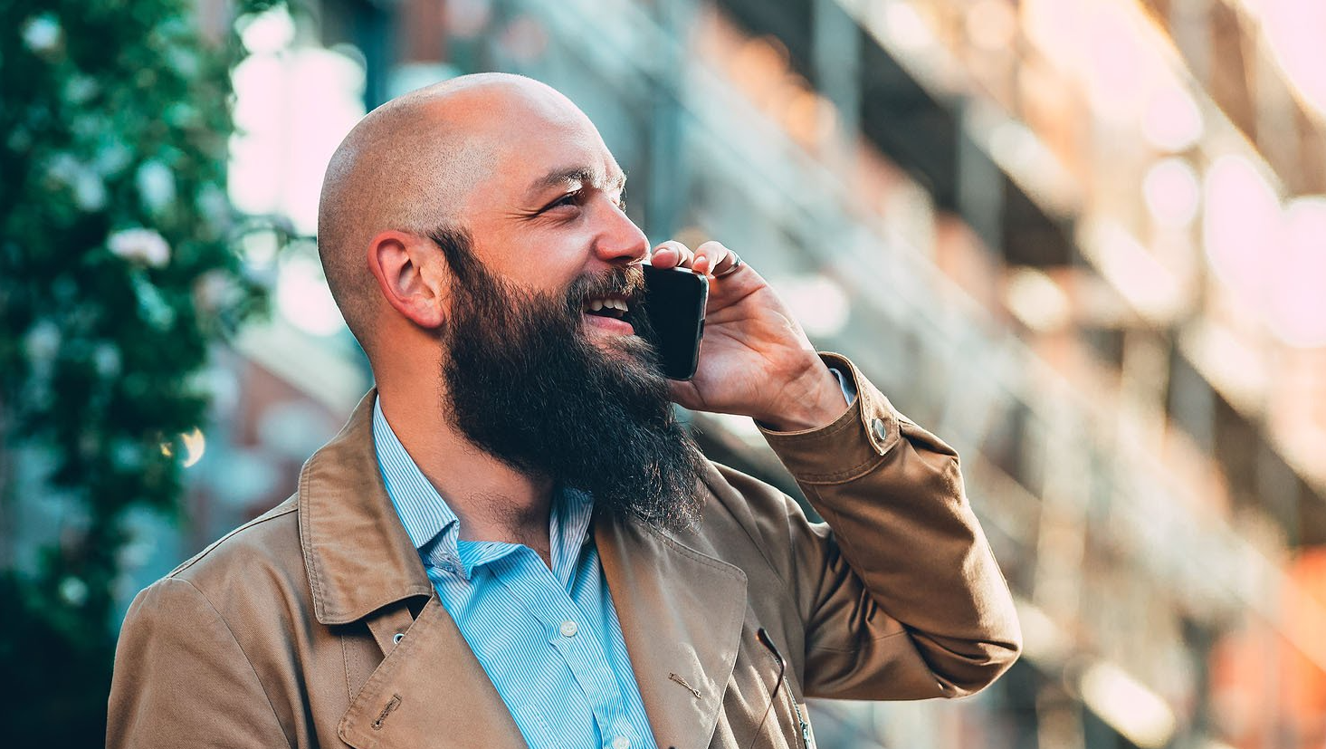 A bald man with a beard is talking on a cell phone.