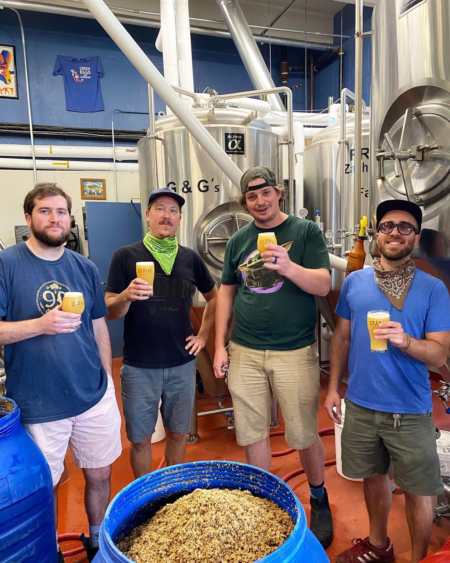 A group of men are standing in a brewery holding cups of beer.