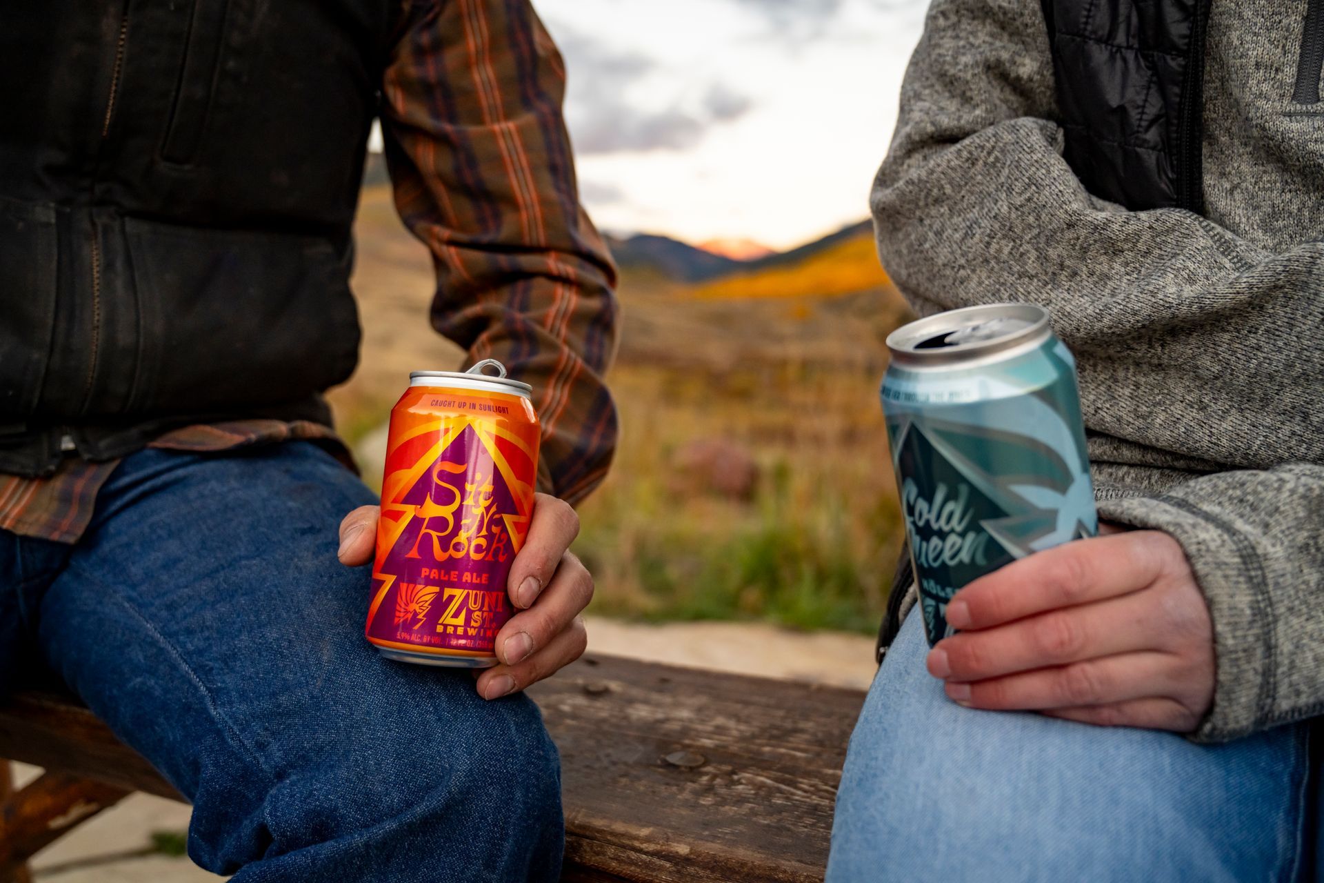 A man and a woman are sitting on a bench holding cans of beer.
