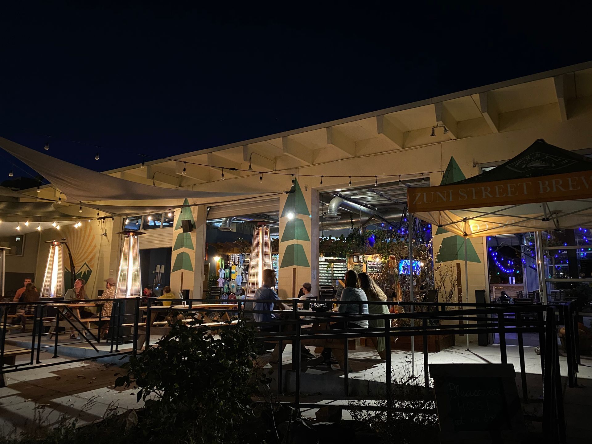 A group of people are sitting at tables outside of a restaurant at night.