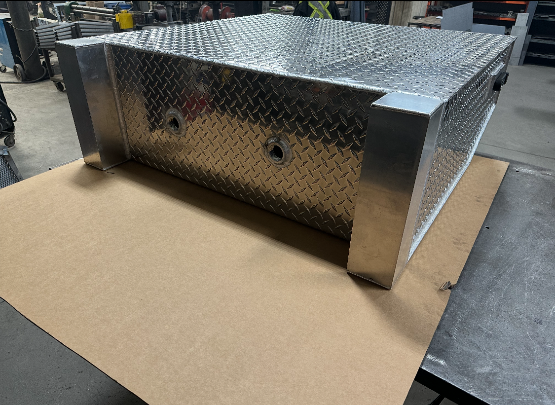 Boîte à outils en aluminium à plaque diamantée, probablement pour un camion, reposant sur du carton sur une surface métallique.