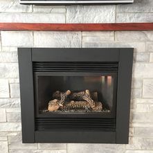 Black fireplace with logs inside, set in a white stone-covered wall. Red shelf above.