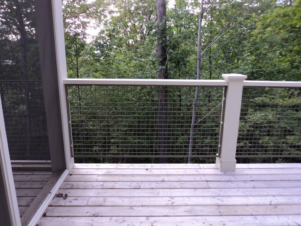 Wooden deck with wire railing overlooking a green forest.