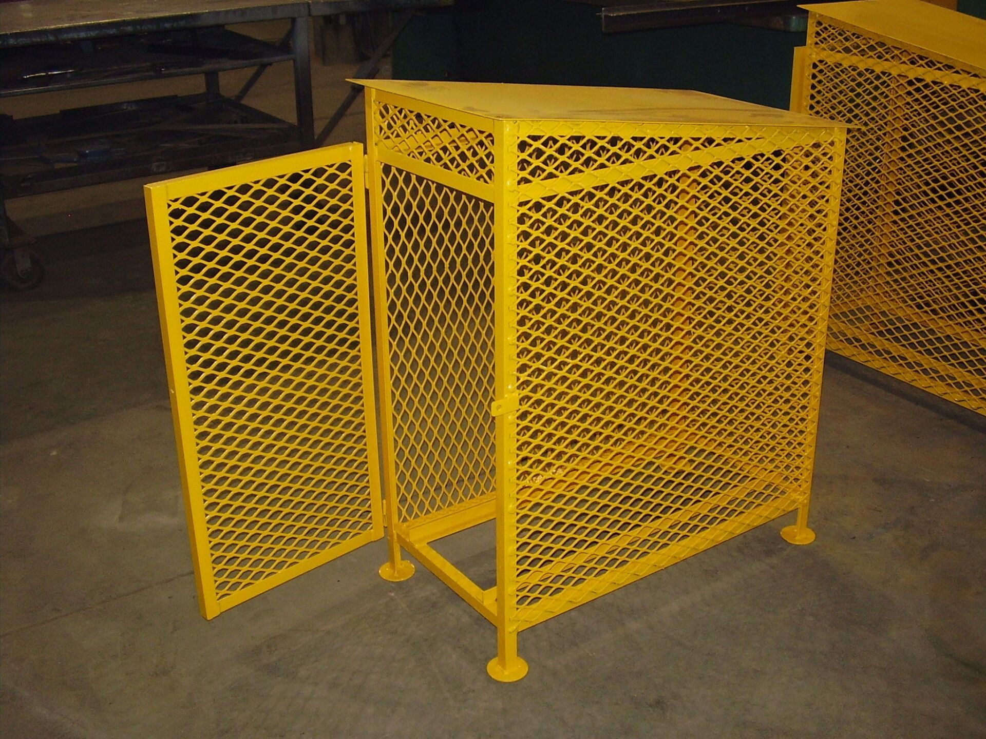 Yellow metal mesh storage cage with door open on concrete floor.