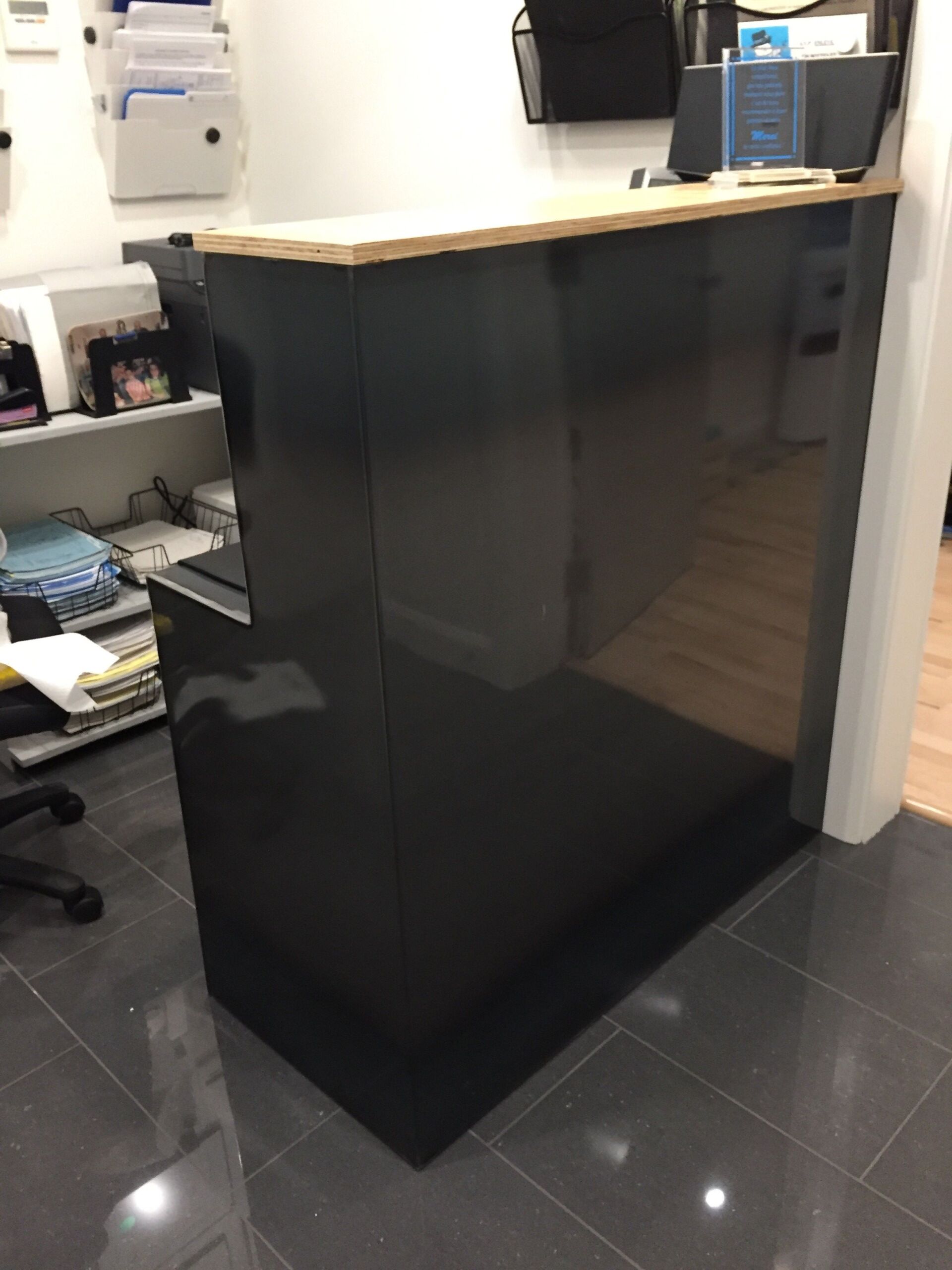 Comptoir de réception noir brillant avec un comptoir en bois clair.