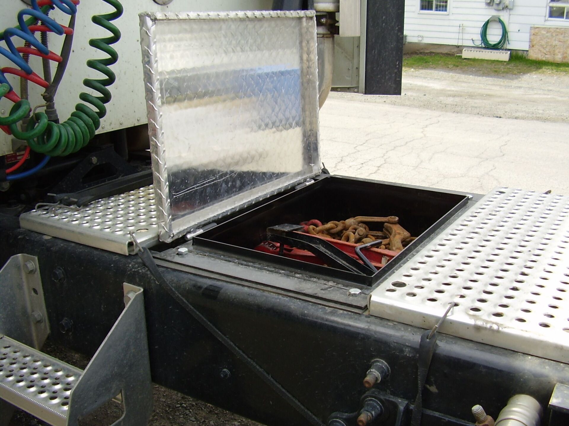Truck storage box with open diamond plate lid, containing chains and gear.