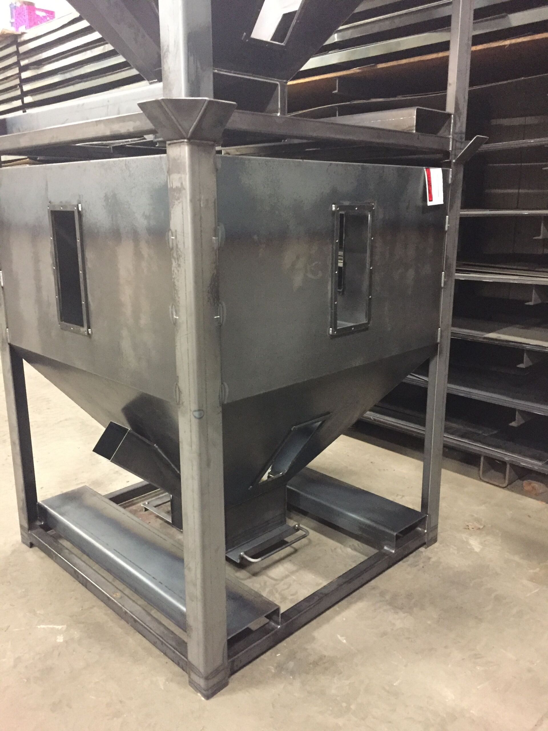 Welded metal hopper with a square frame, rectangular openings, and a tapered bottom section.
