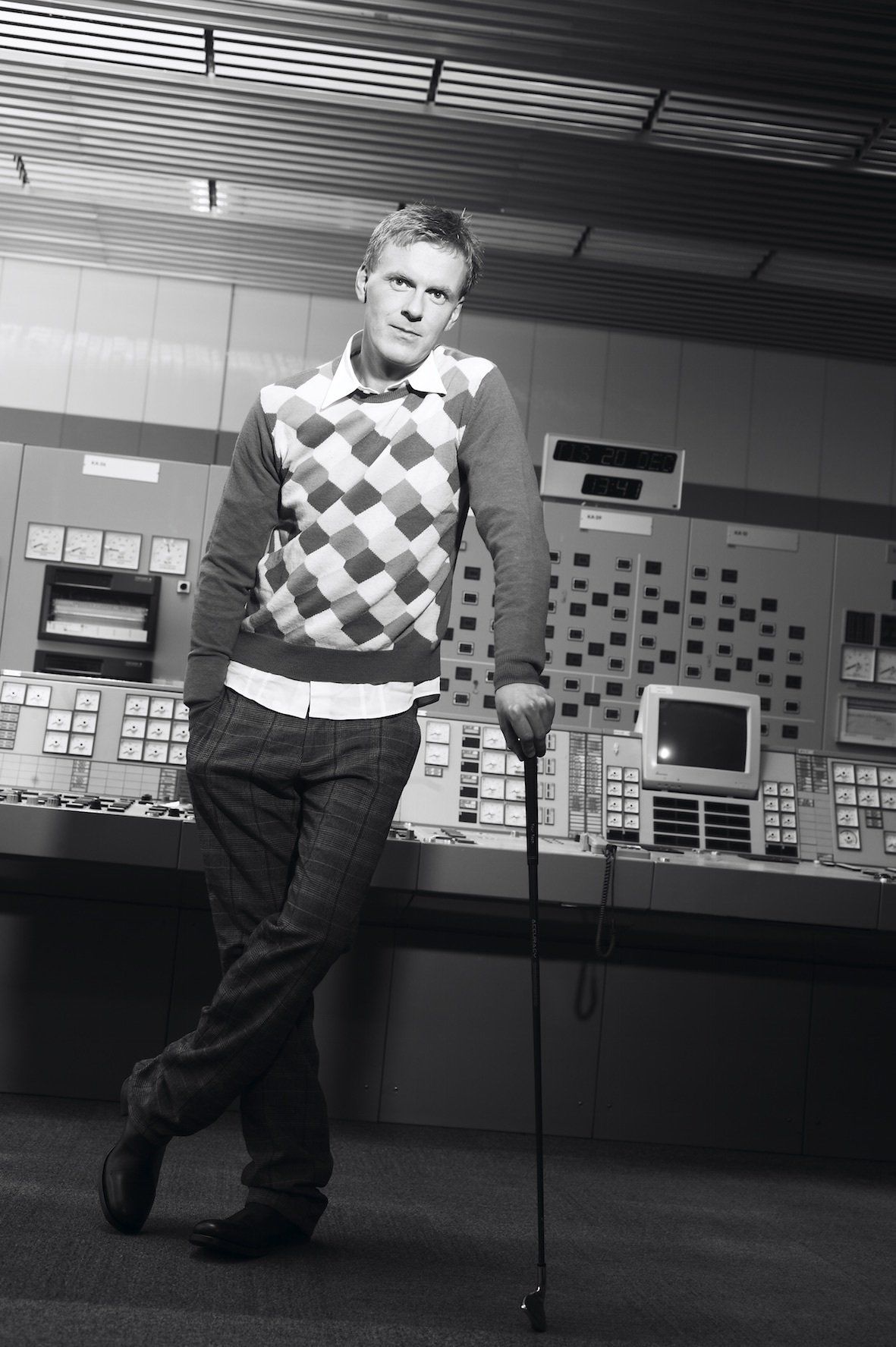 Halfdan E with a golf club, standing in front of a nuclear control panel