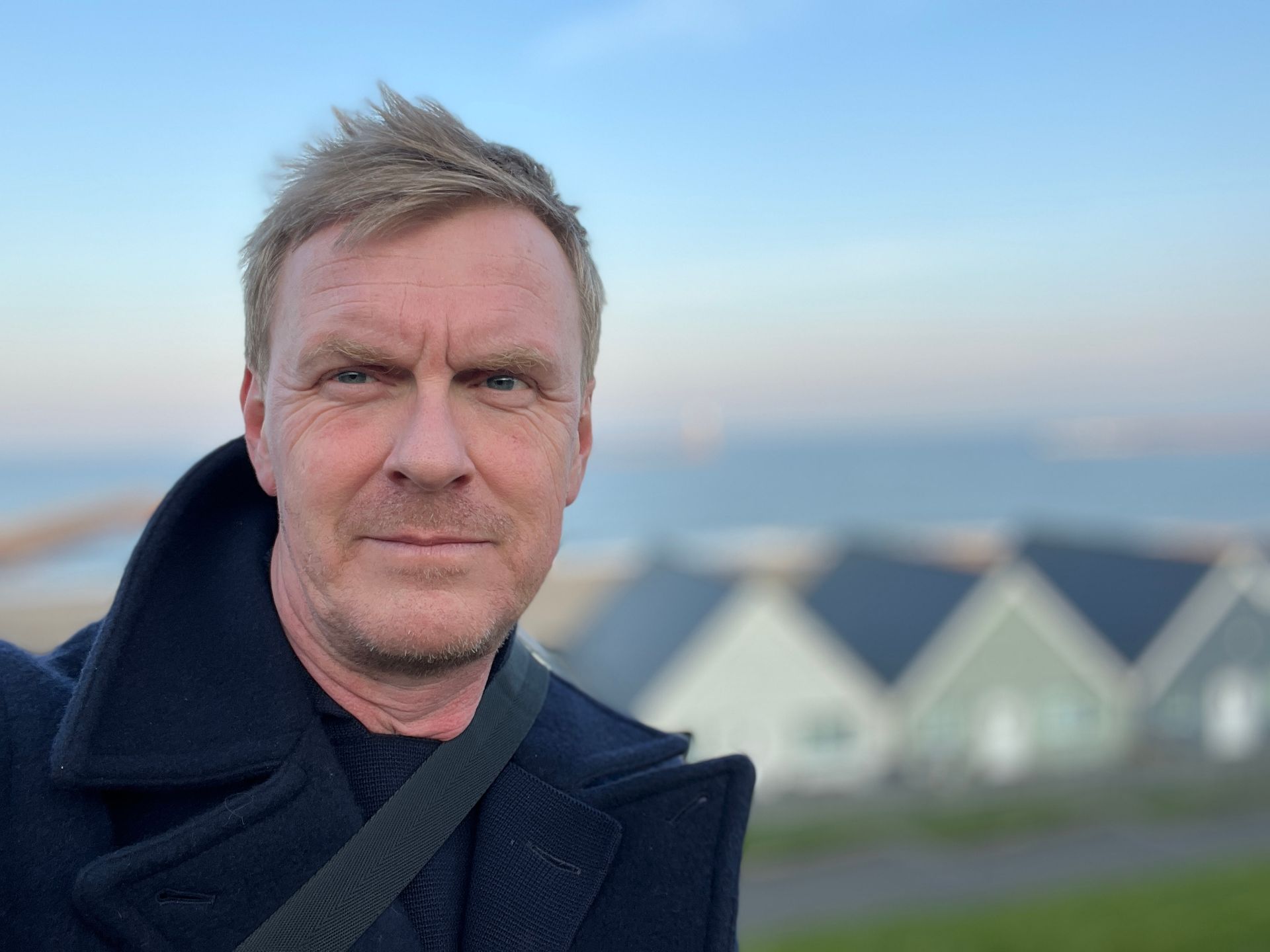 A man in a black coat is standing in front of a row of houses.