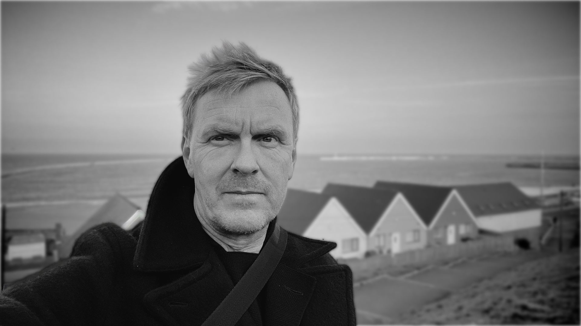 A black and white photo of Halfdan E standing in front of a row of houses