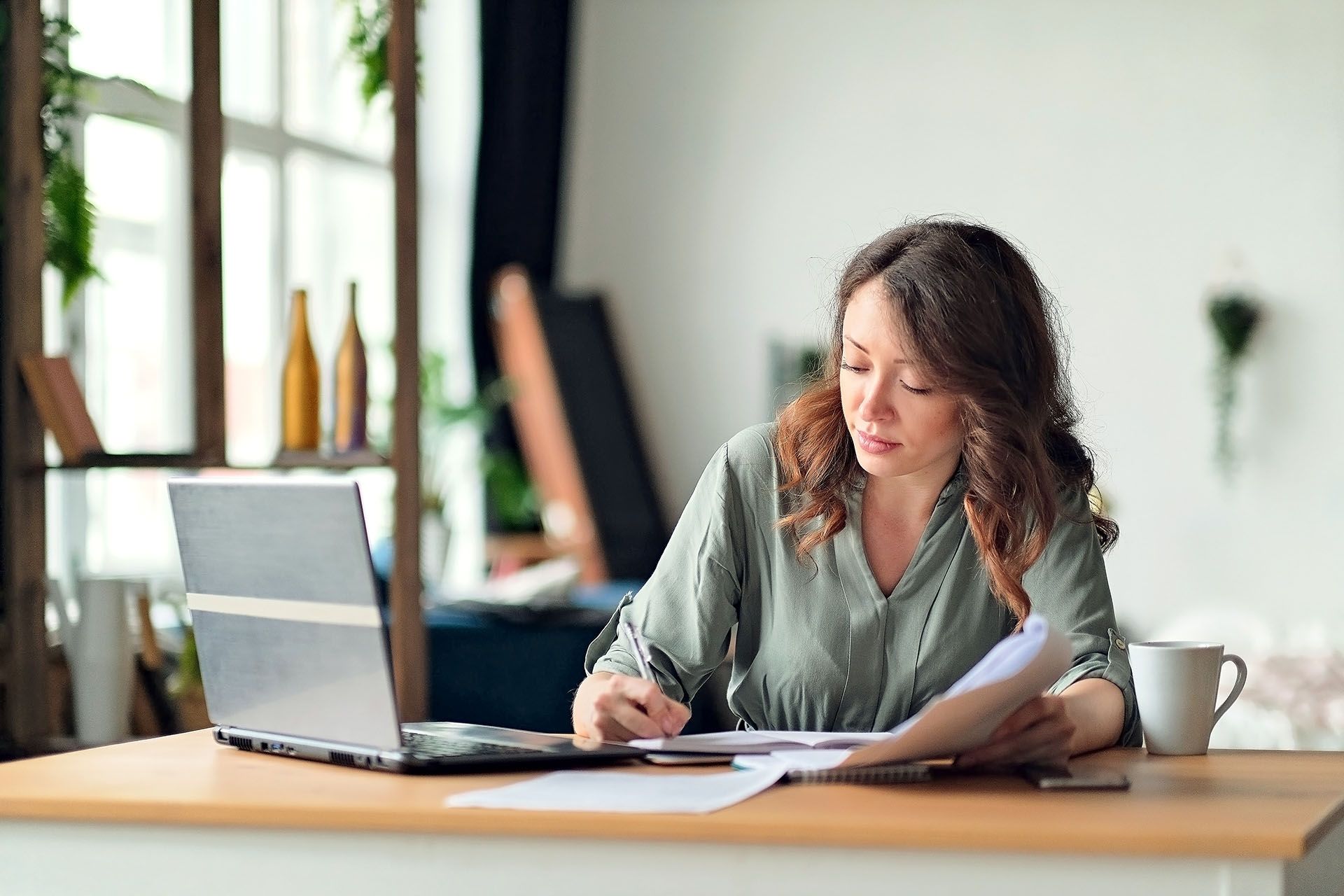 A woman is sitting at a table with a laptop and papers.