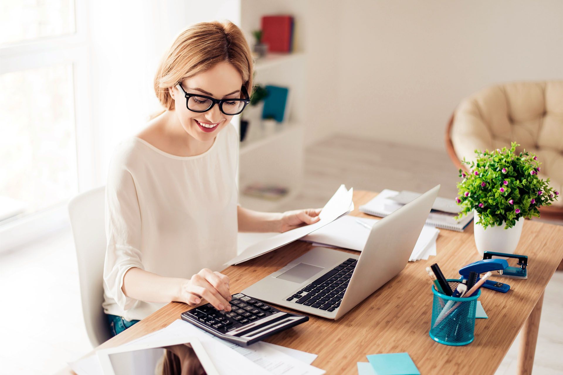 A woman is sitting at a desk with a laptop and a calculator.