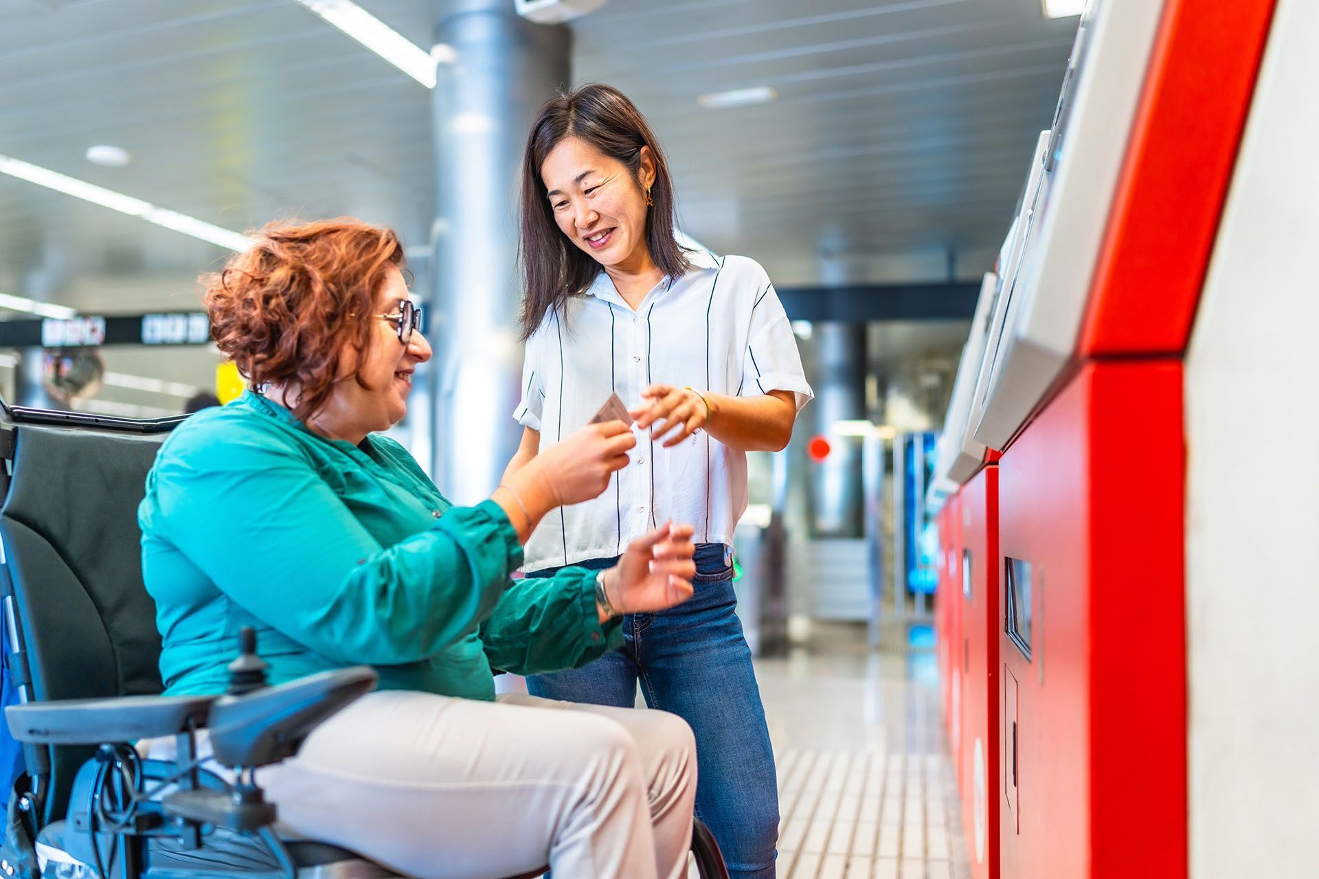 A woman in a wheelchair is talking to another woman at an airport.