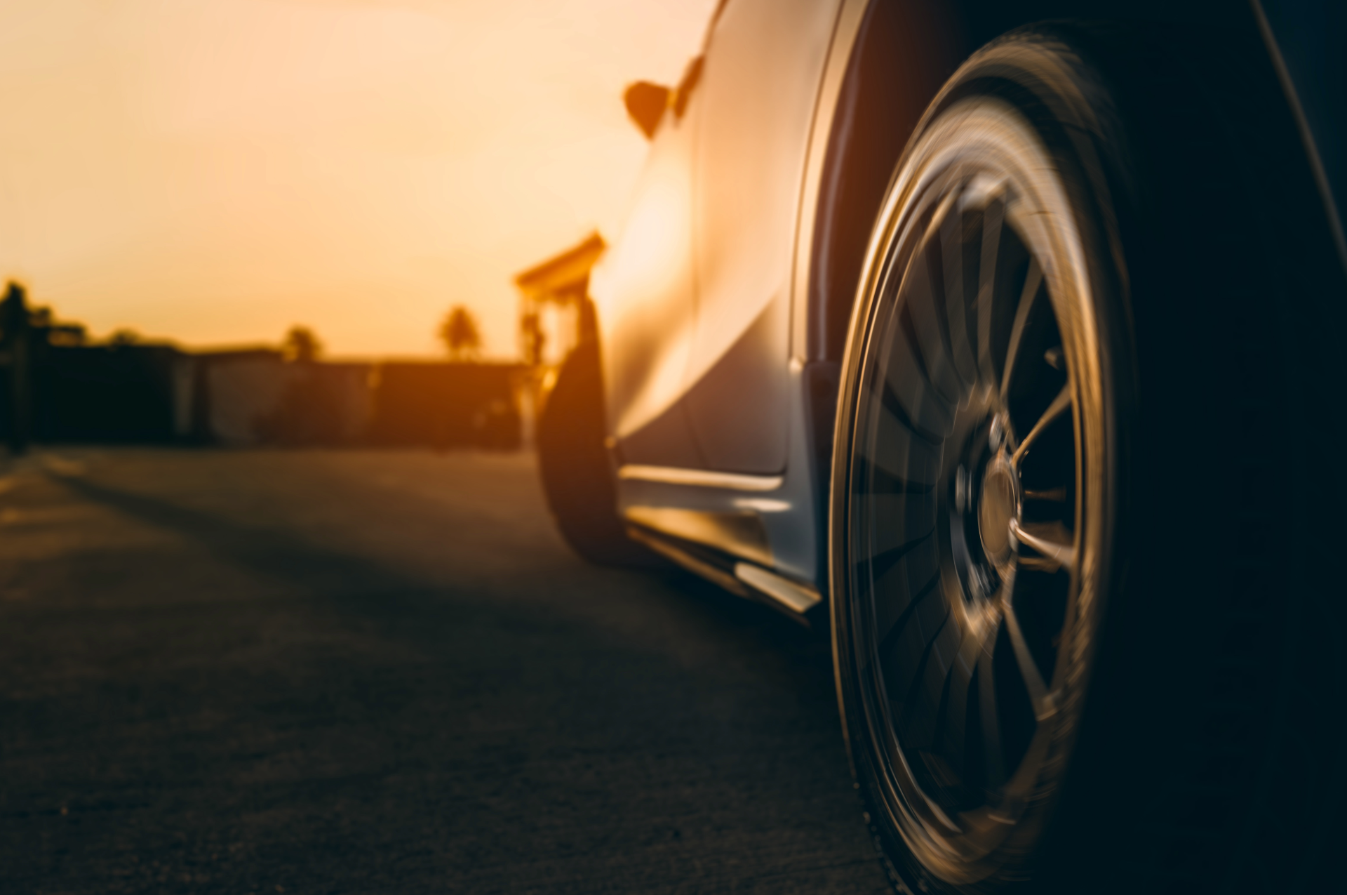 A close-up view of a car wheel on a road during a sunset, casting a warm golden glow over the scene.