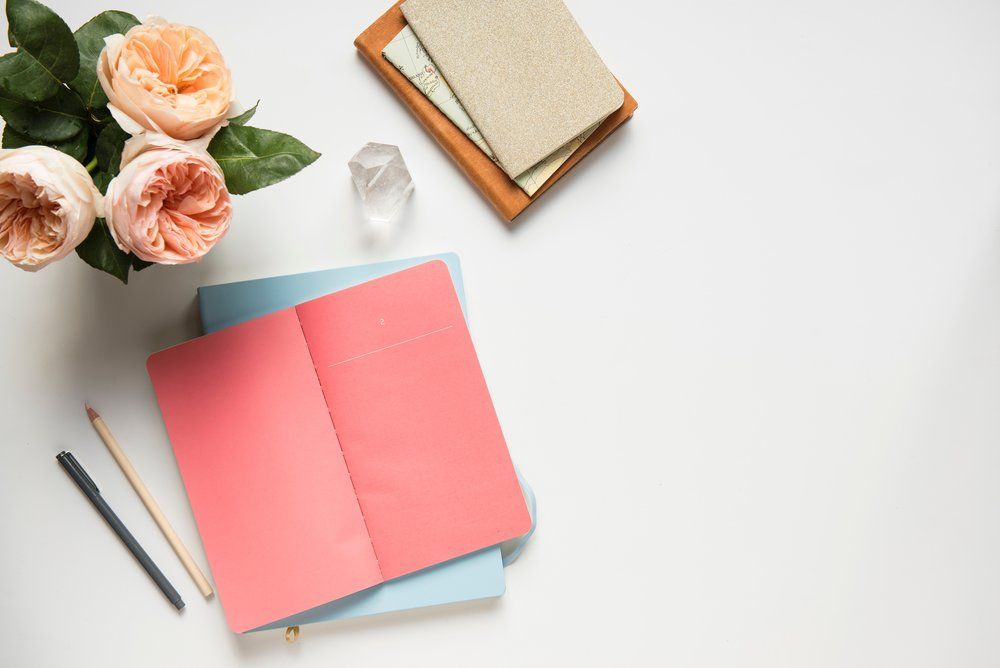 A stack of notebooks, pencils, flowers and crystals on a white table.