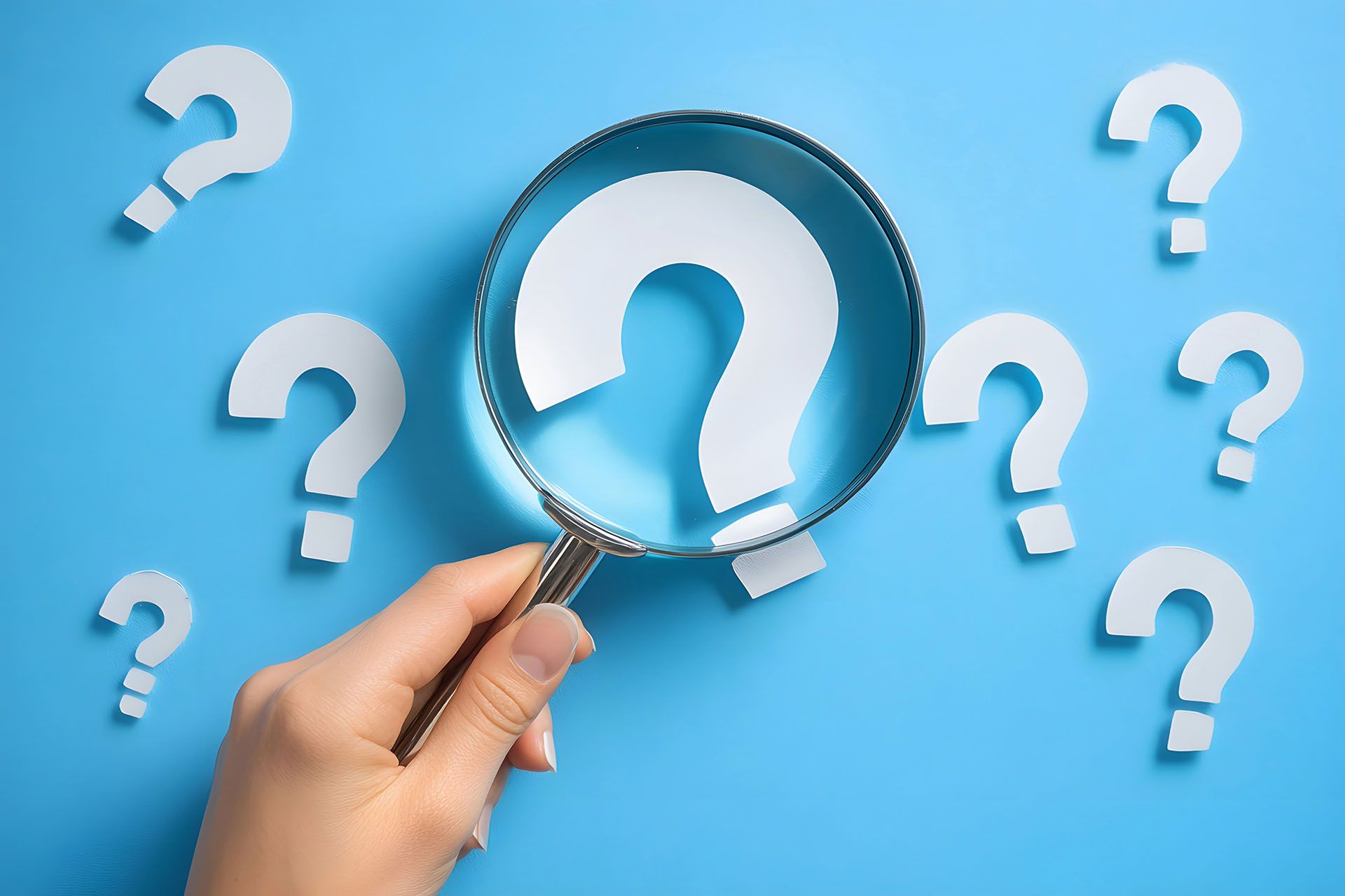A hand is holding a magnifying glass with a question mark cut out of it.