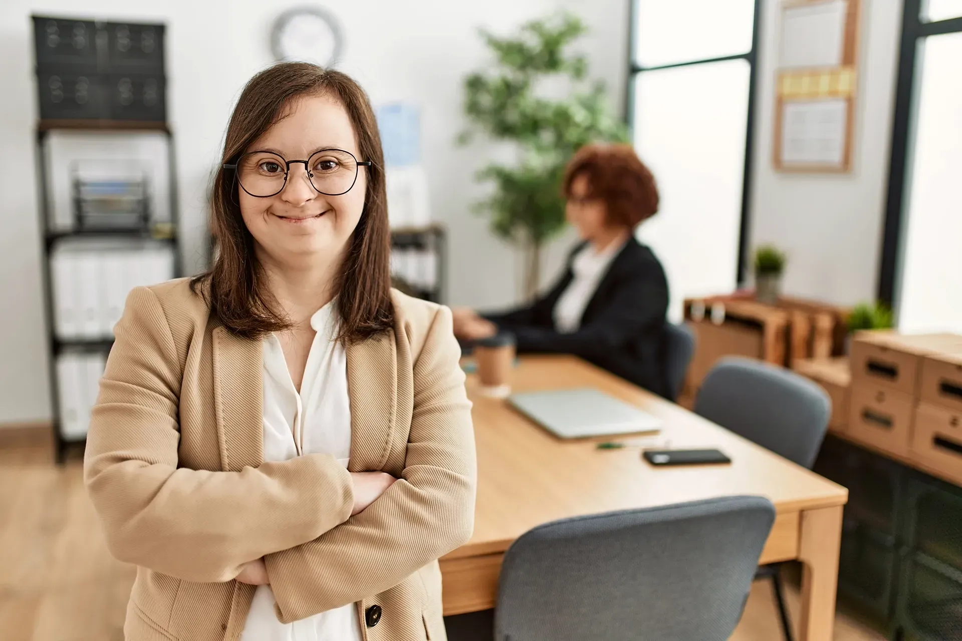 A woman is standing in an office with her arms crossed and smiling.