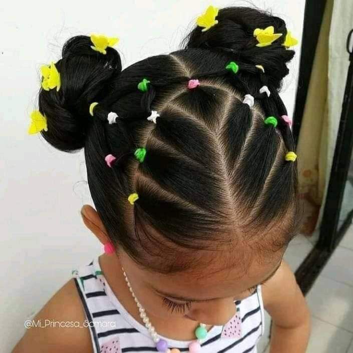 Ein kleines Mädchen trägt ein gestreiftes Hemd und eine Halskette und hat die Haare zu zwei Knoten gebunden.