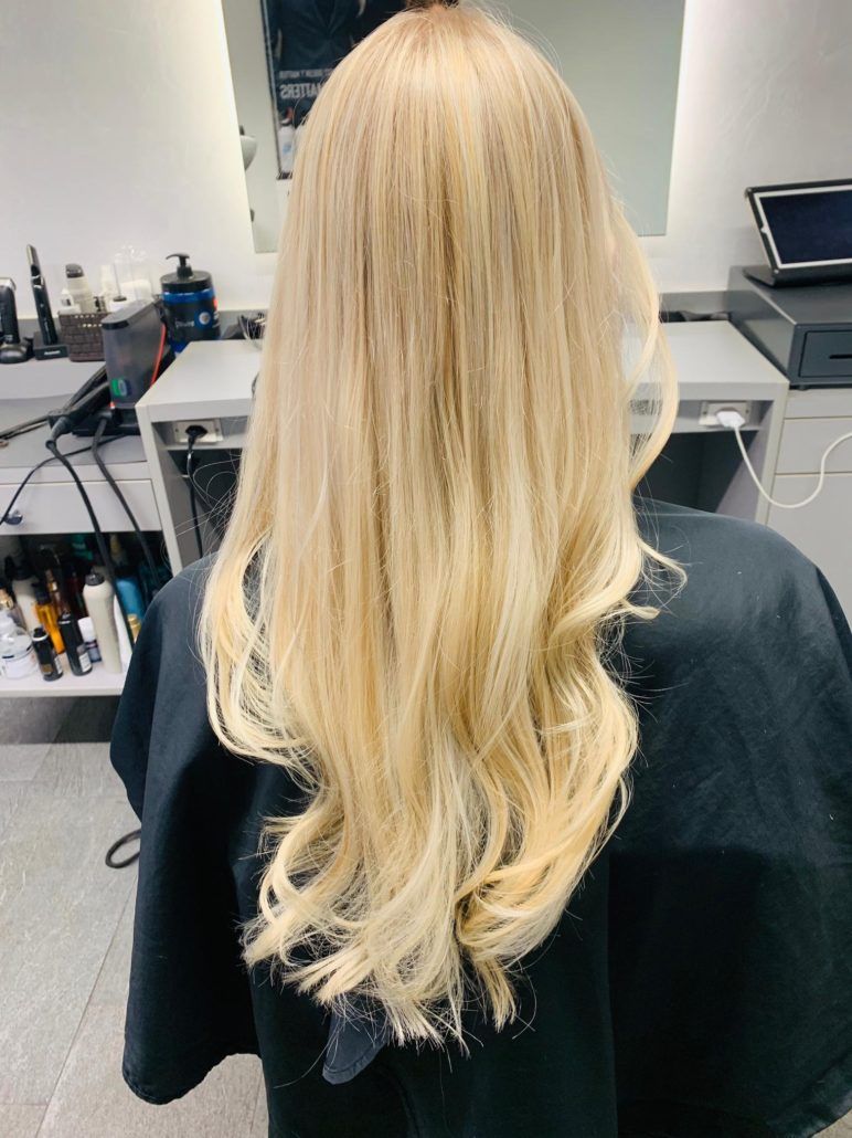 Eine Frau mit langen blonden Haaren sitzt auf einem Stuhl in einem Salon.