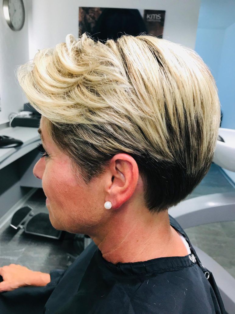 Eine Frau mit kurzen blonden Haaren sitzt auf einem Stuhl in einem Salon.