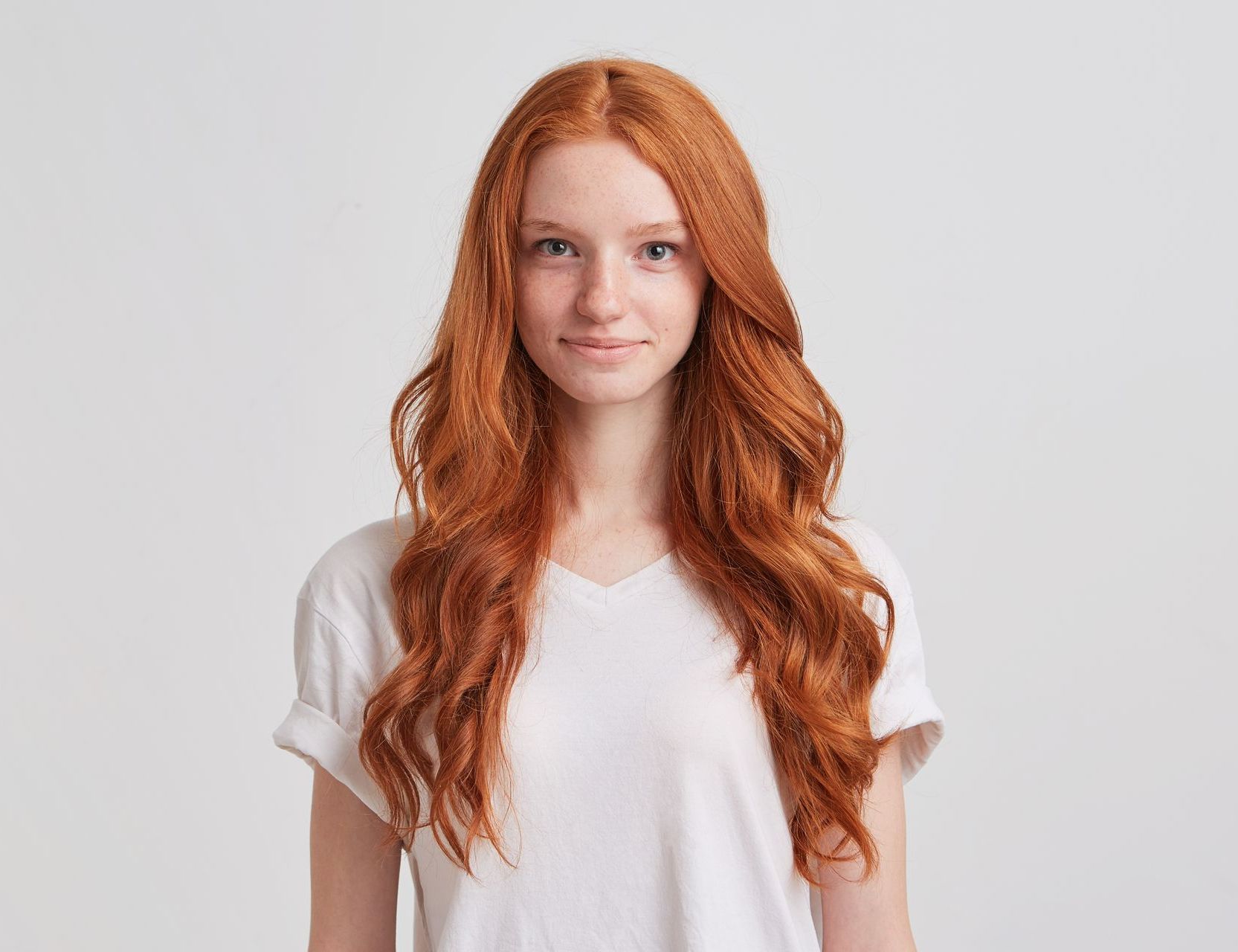 Eine junge Frau mit langen roten Haaren trägt ein weißes T-Shirt.