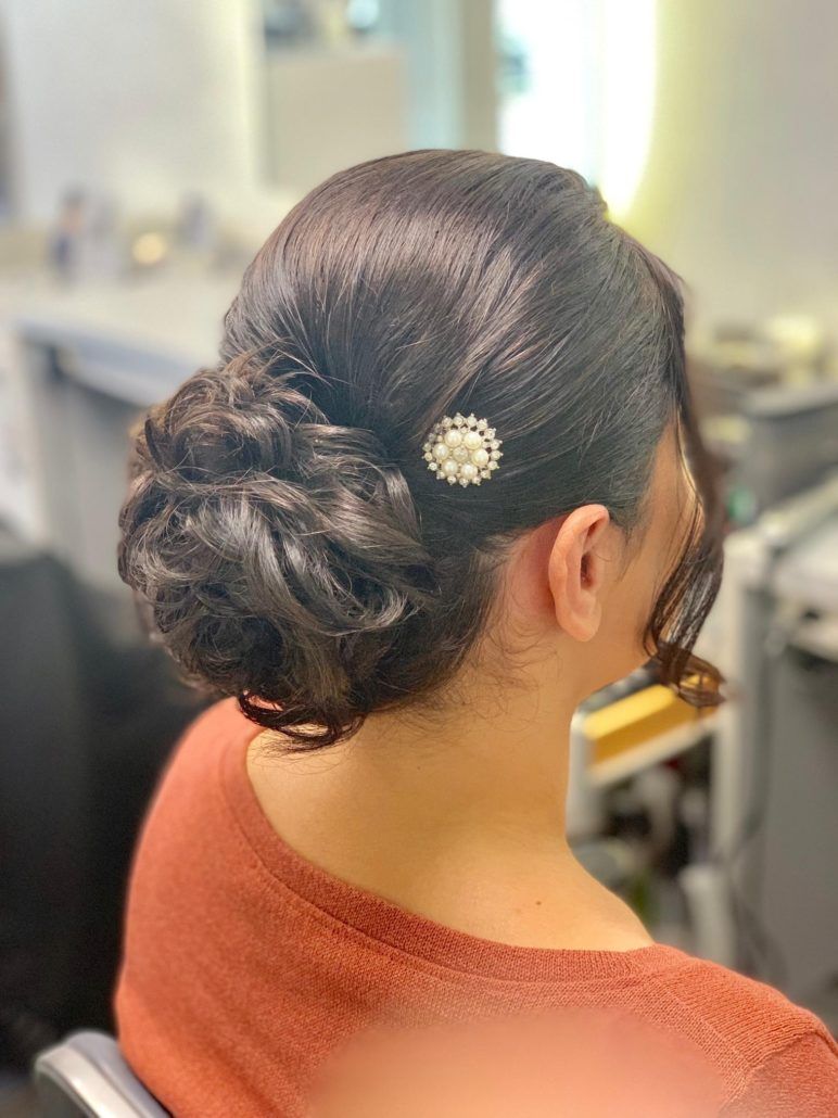 Eine Frau sitzt auf einem Stuhl und hat die Haare zu einem Knoten zusammengebunden.