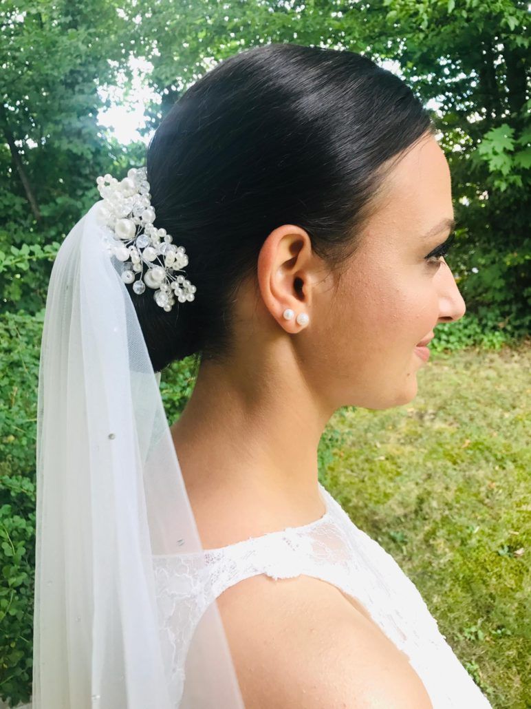 Eine Braut mit Schleier und Ohrringen steht auf einem Feld.