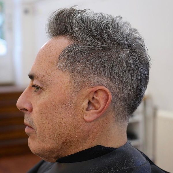 Ein Mann mit grauem Haar lässt sich von einem Friseur die Haare schneiden.