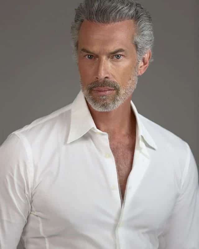 Ein Mann mit grauen Haaren und Bart trägt ein weißes Hemd.