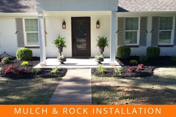 Front yard with walkway, porch, potted plants, and fresh mulch and rock landscaping in front of a white house