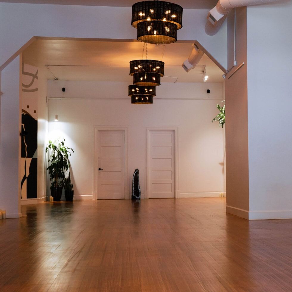 Empty modern gallery room with wooden floors, white walls, and hanging chandeliers