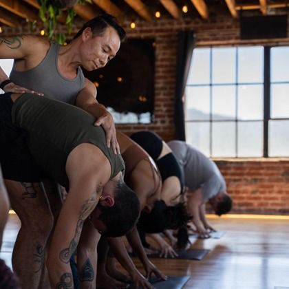 Yoga class stretching in a sunlit studio, with several people bending forward in a line