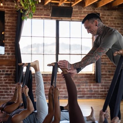 Yoga instructor assisting students in a brick studio with large windows