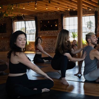 People practicing yoga in a brick studio with wooden floors and large windows.