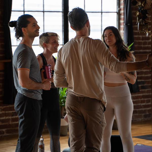 Four people talking in a sunlit studio with brick walls and large windows