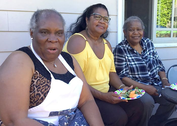 Three women are sitting on a porch holding plates of food