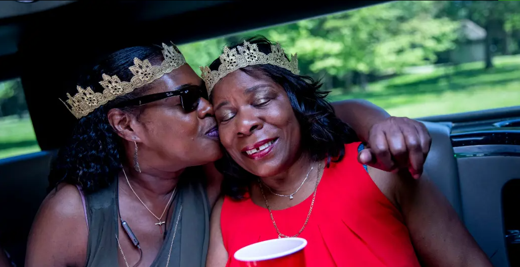 Two women wearing crowns are kissing in a car.