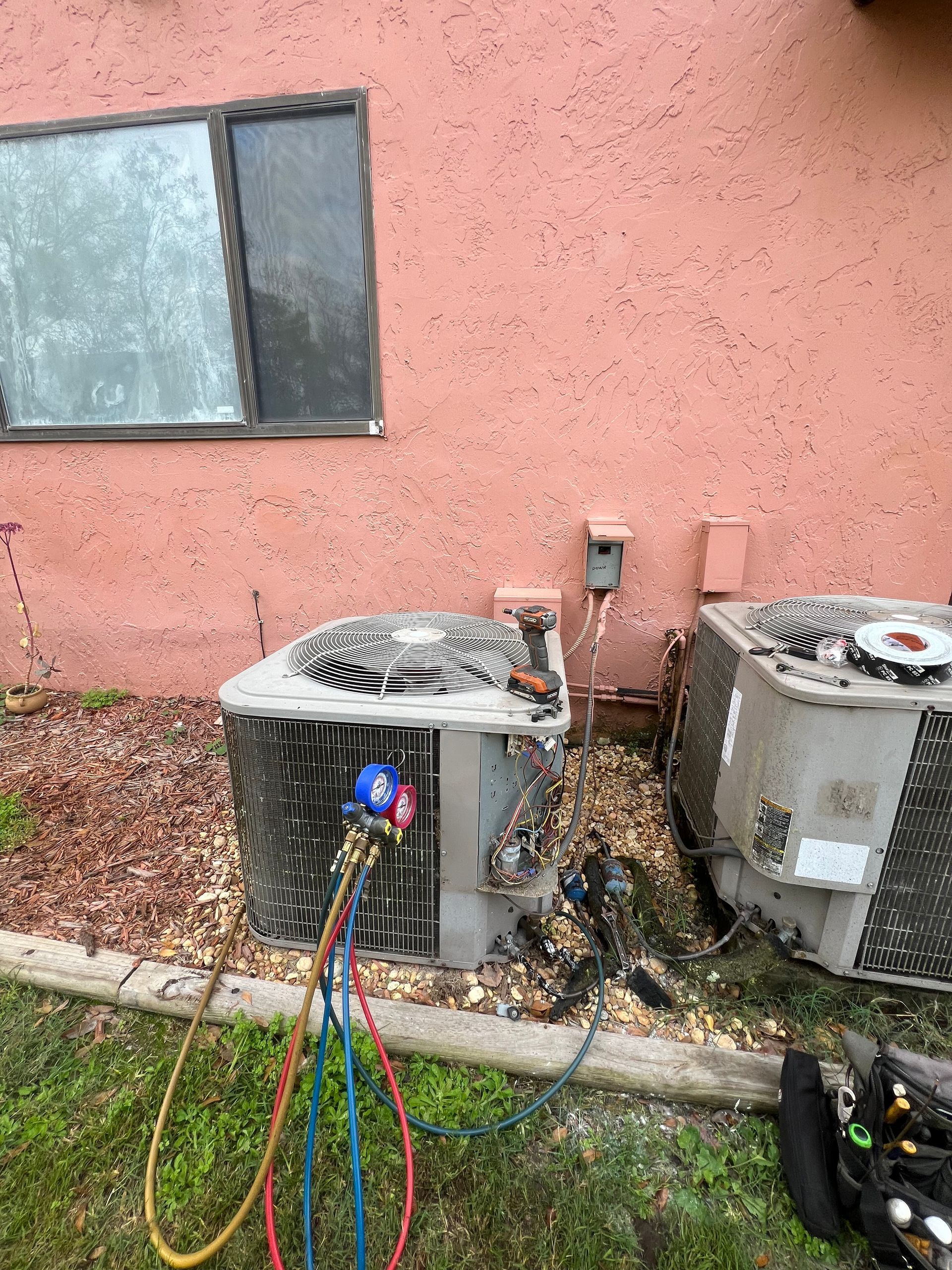 two air conditioners are sitting next to each other on the side of a building .