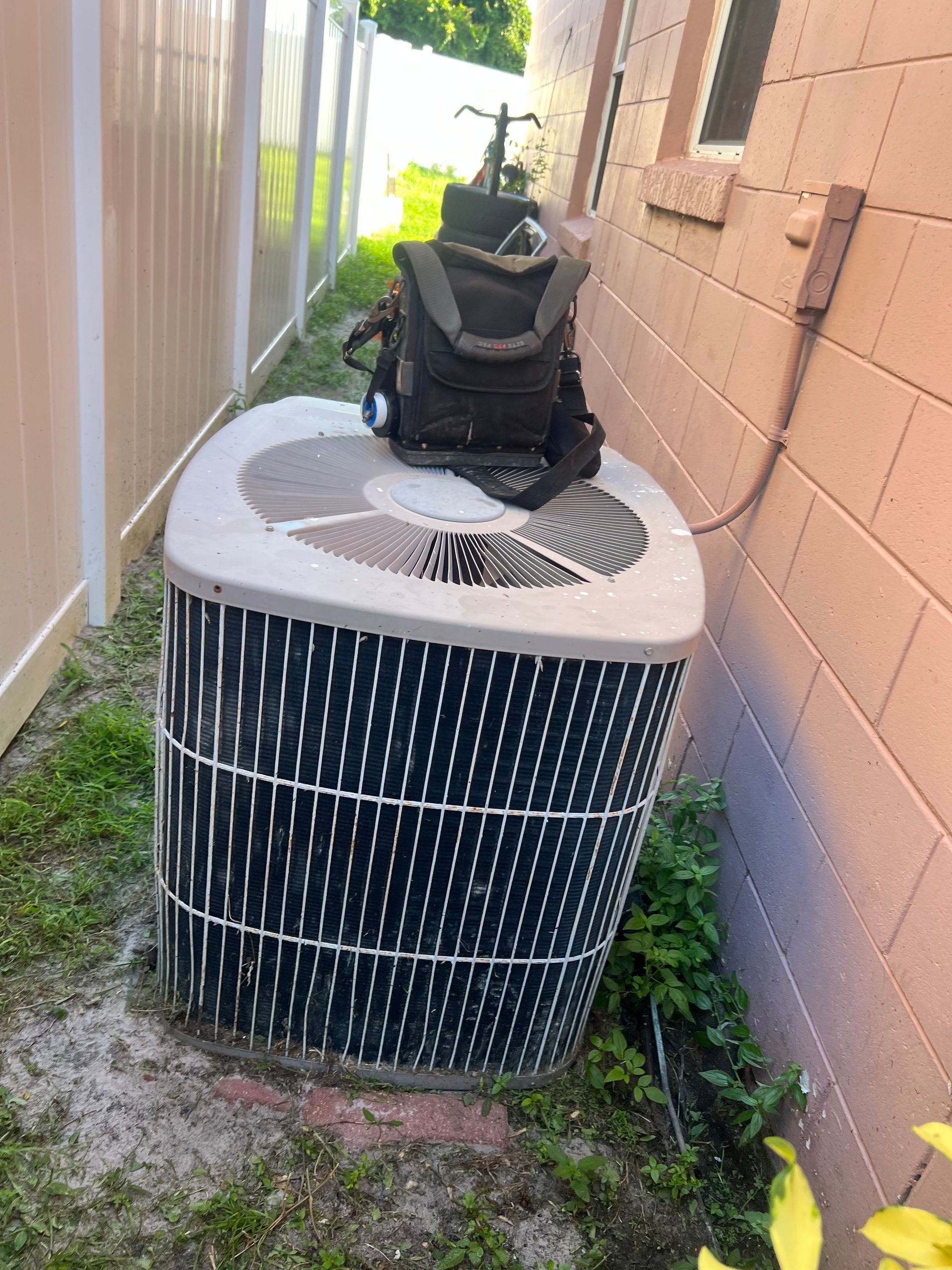 an air conditioner is sitting on the side of a building next to a fence .