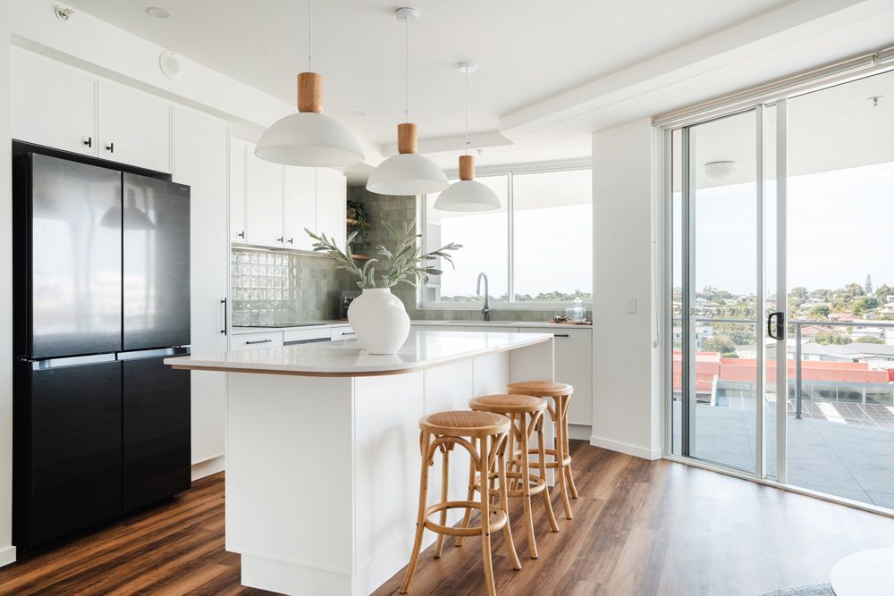 Bright modern kitchen with white island, black fridge, wooden stools, and sliding doors to a deck. — Reynolds Built In Caloundra, QLD