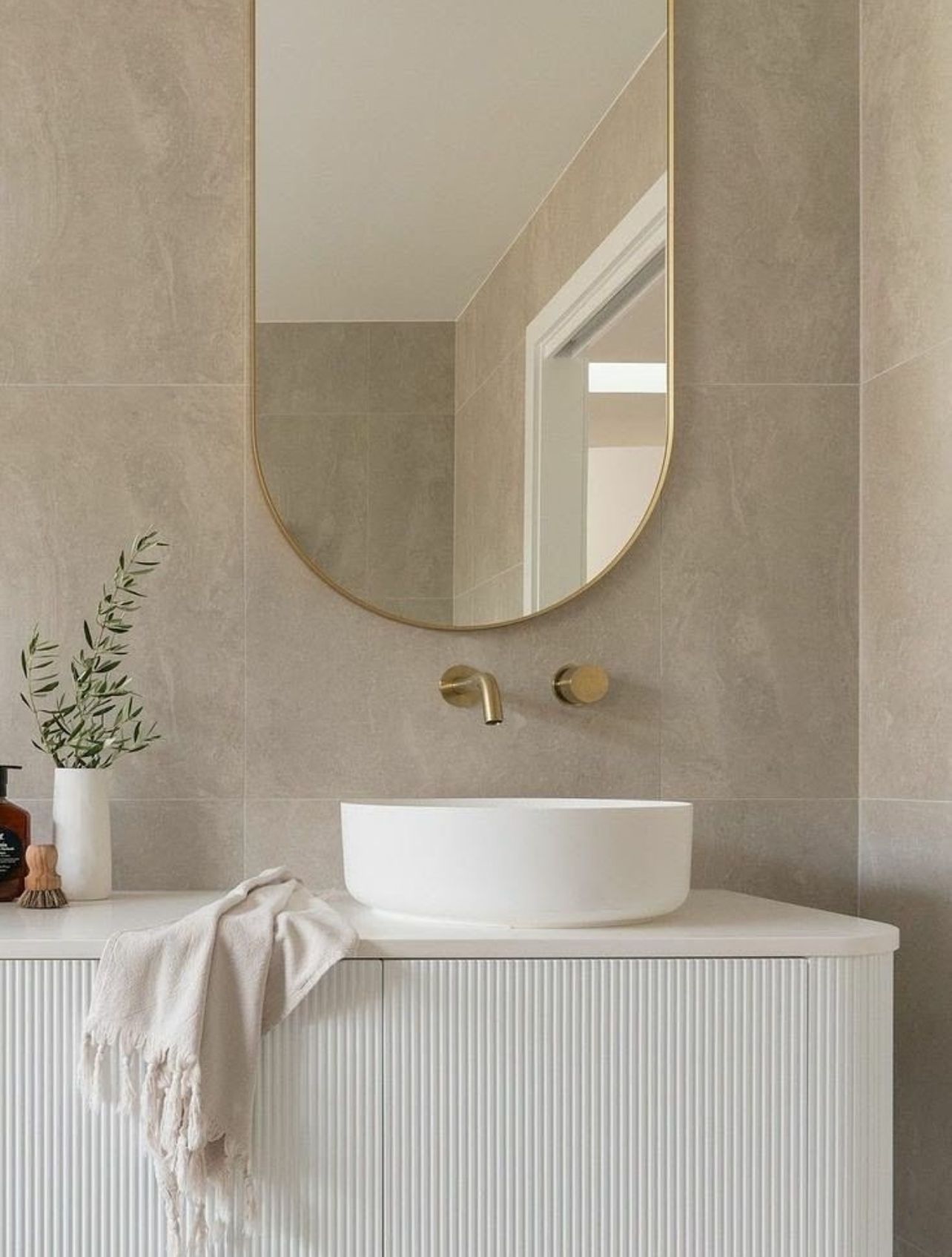 Minimal beige bathroom vanity with round mirror, white vessel sink, and brass faucet on ribbed cabinet — Reynolds Built In Caloundra, QLD