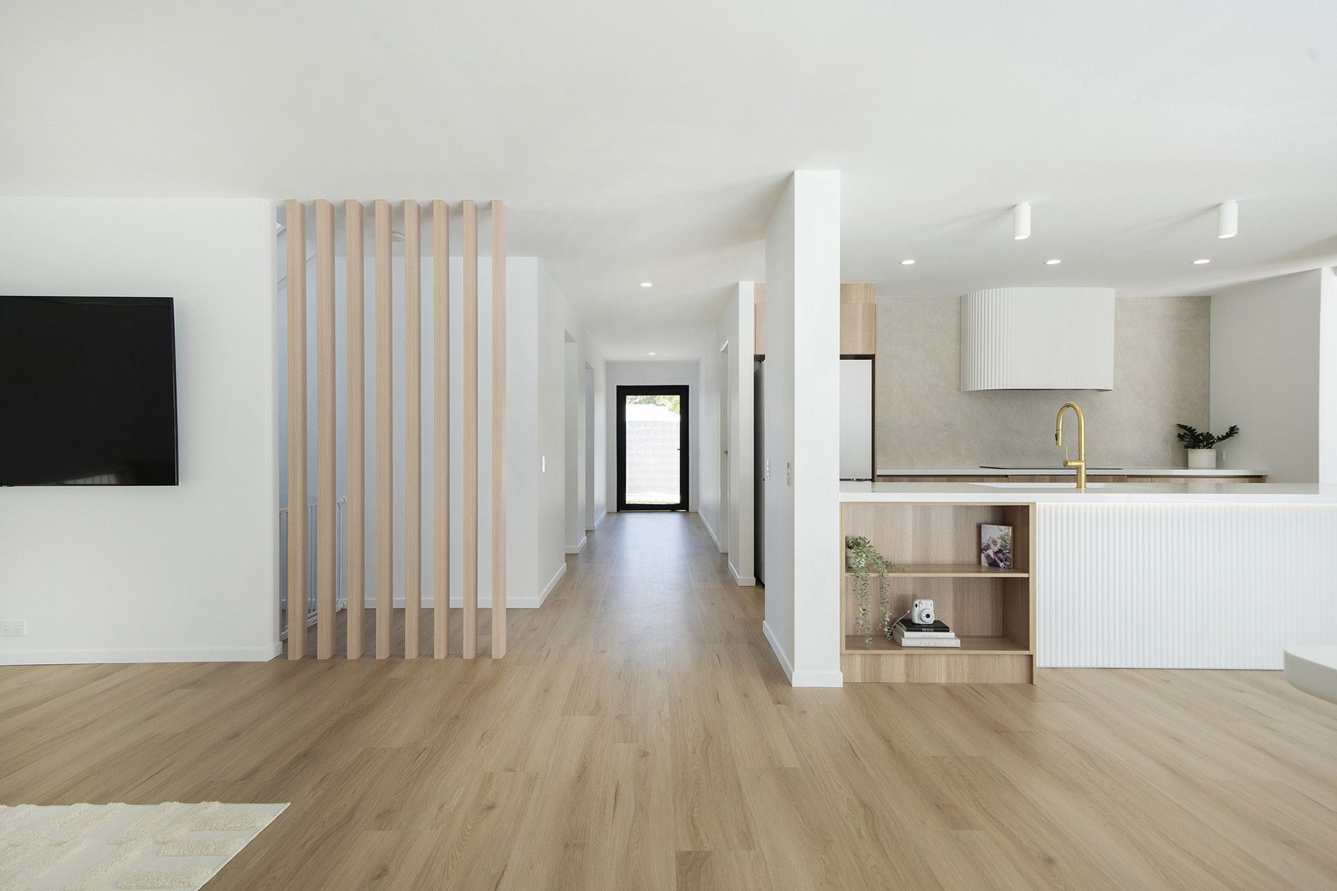A bright, open-plan interior featuring light wood flooring, a slatted wooden divider, and a modern kitchen.