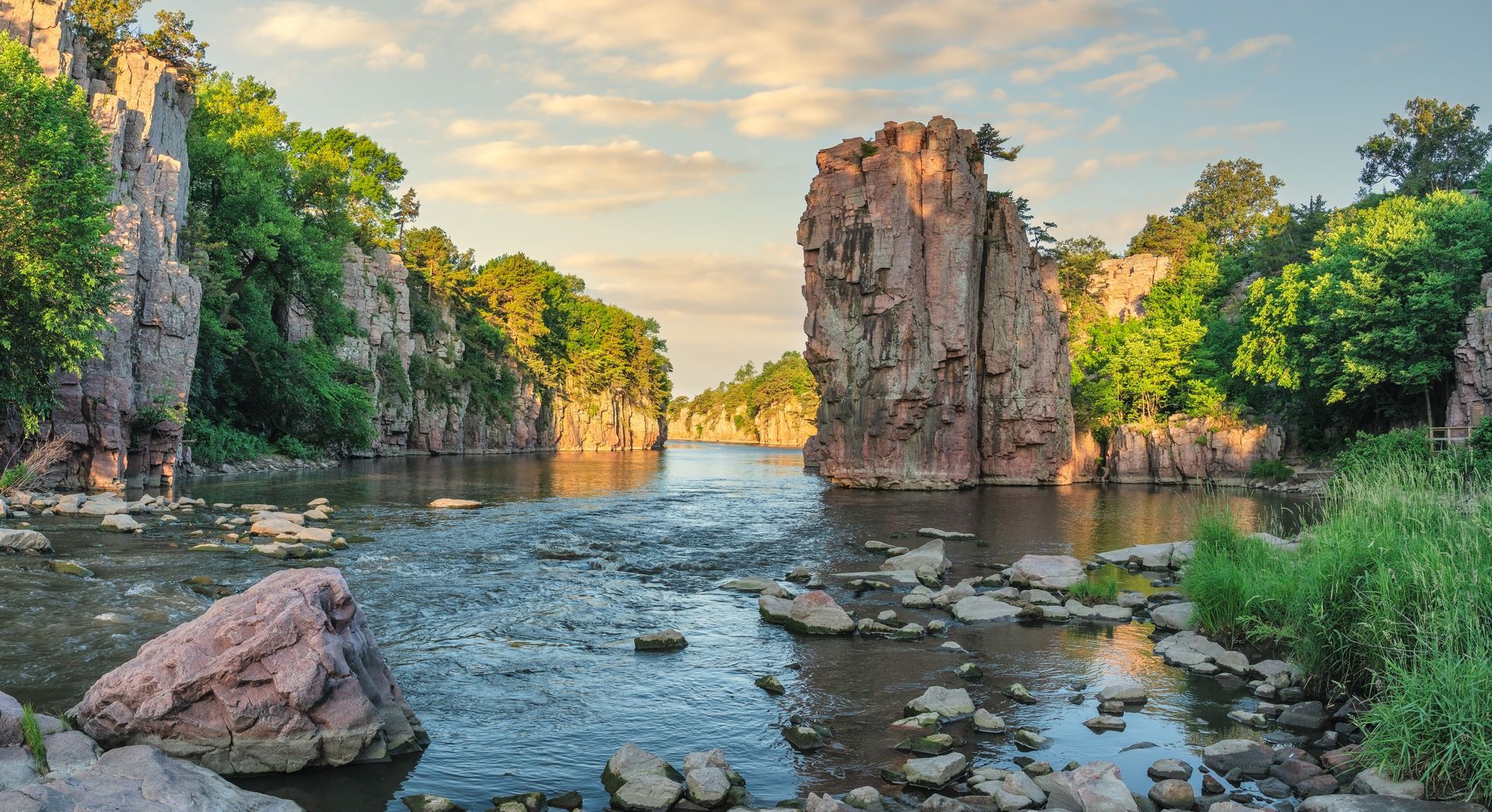 River flows between pink rock formations under a cloudy sky.