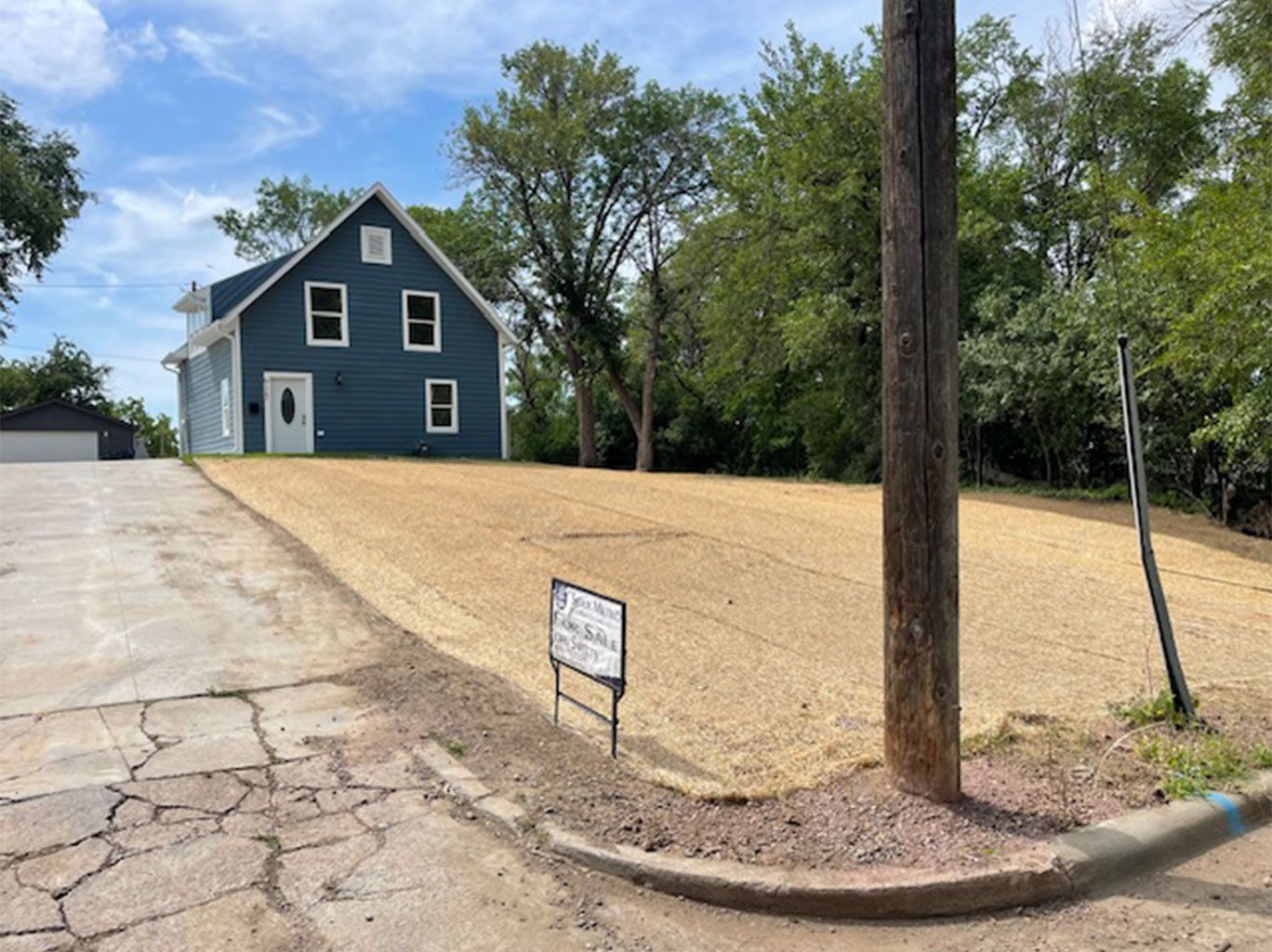 Blue house with a freshly seeded yard and a utility pole.