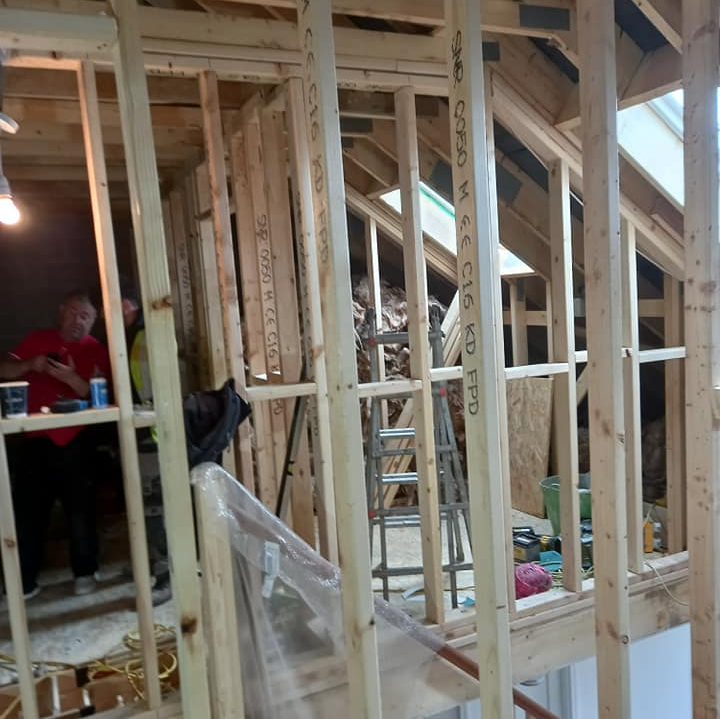 Interior framing of a building under construction. Workers in red shirts are visible.