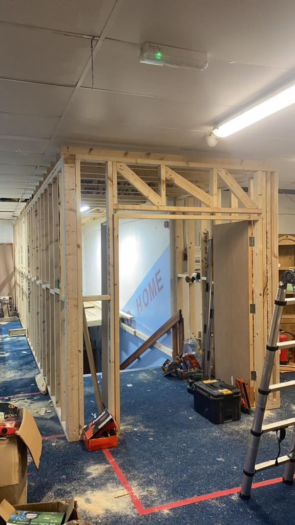Interior construction site with wooden frame walls, open doorway, tools, and blue carpet.